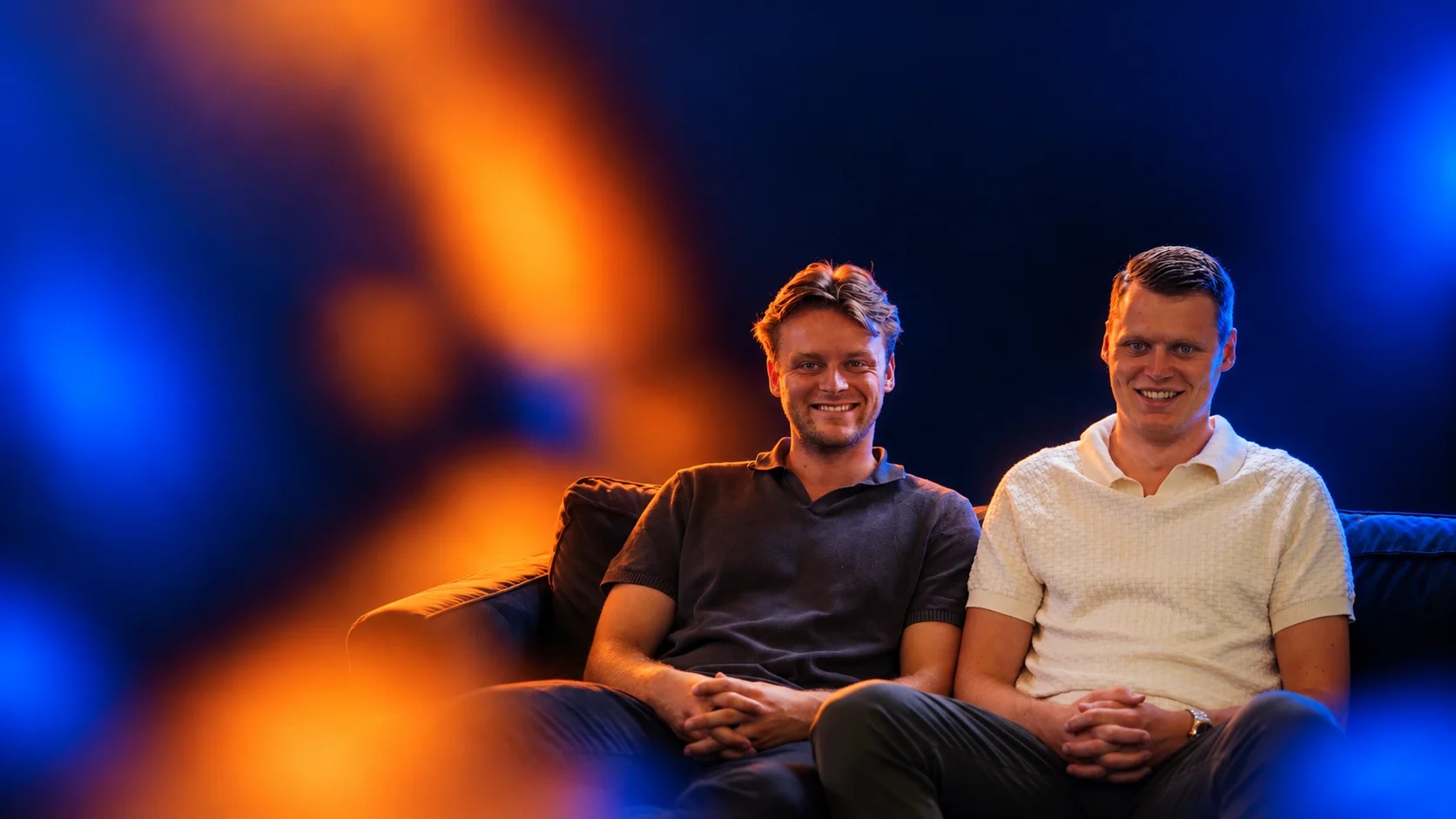 Portret van de twee oprichters van Salesnerds in oranje en blauw licht